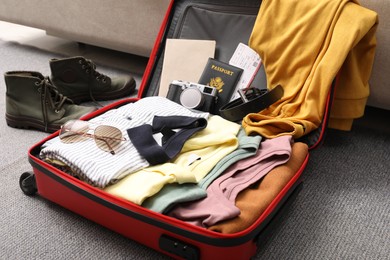 Photo of Open suitcase with clothes, accessories and shoes on floor indoors, closeup