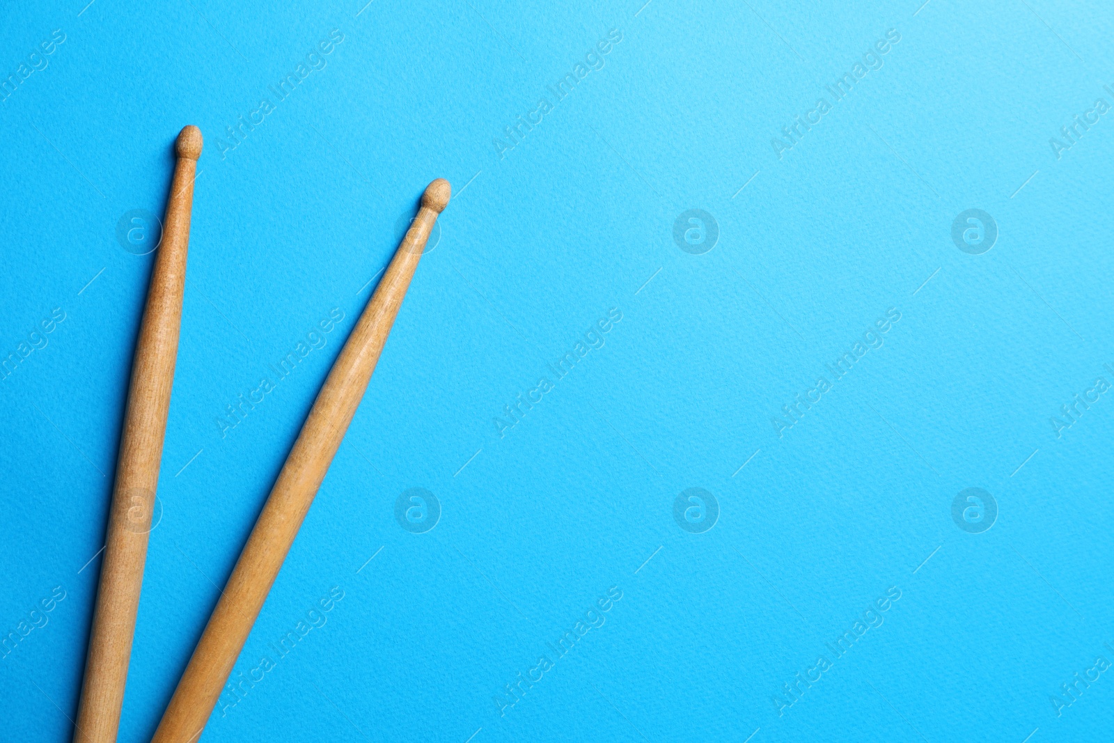 Photo of Two wooden drum sticks on light blue background, top view. Space for text