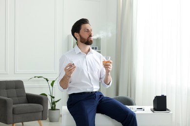 Photo of Man using cigarette holder for smoking and holding glass of whiskey in office