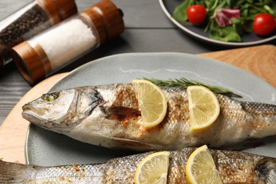 Delicious baked fish, lemon and rosemary on grey wooden table, closeup