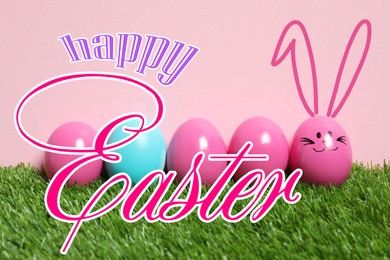 Image of Happy Easter. One egg with drawn face and ears as bunny among others on green grass against pink background