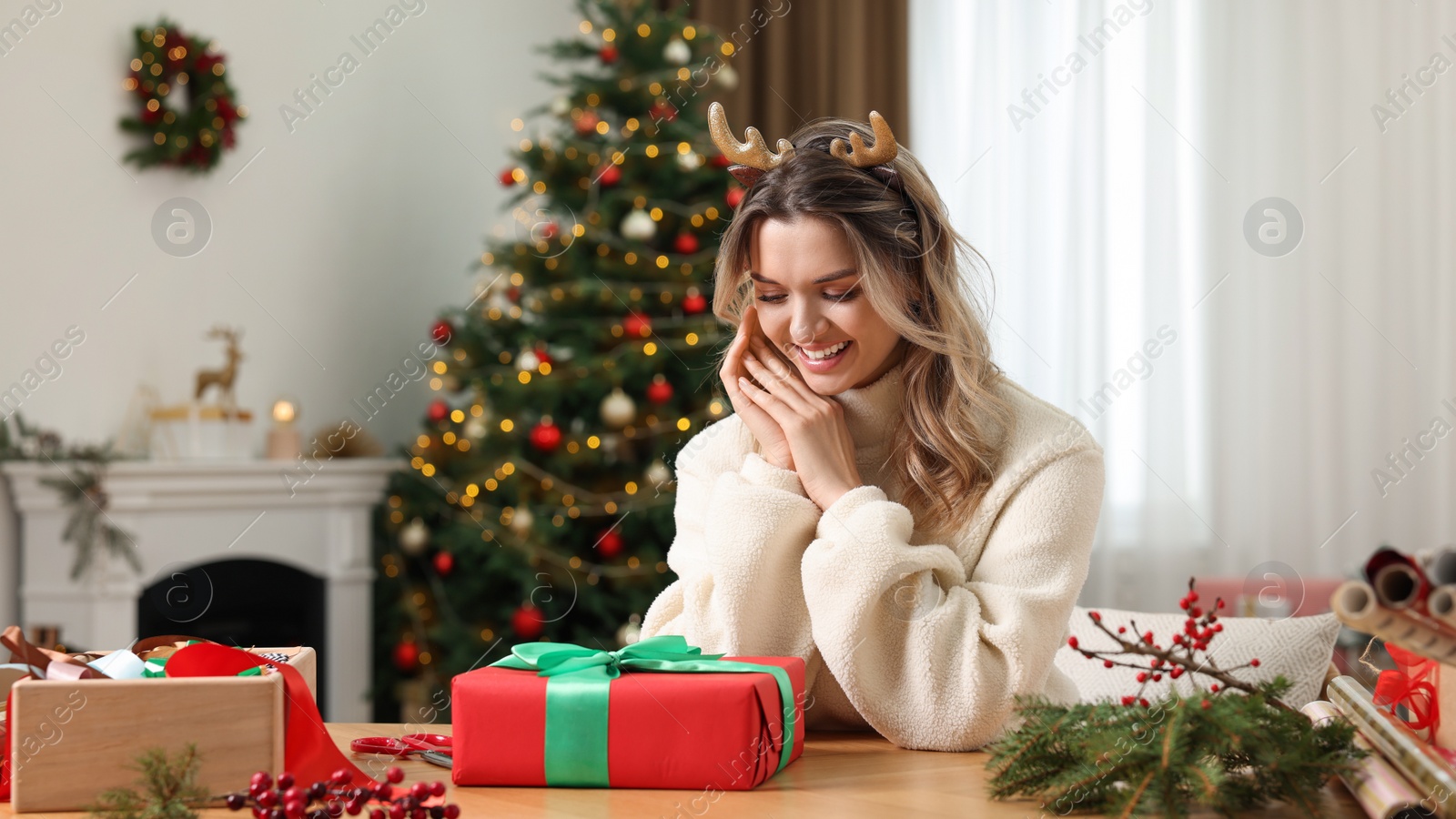 Photo of Young woman with beautifully wrapped Christmas gift at home