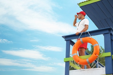 Photo of Male lifeguard on watch tower against blue sky
