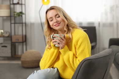 Beautiful woman in stylish warm sweater holding cup of drink at home