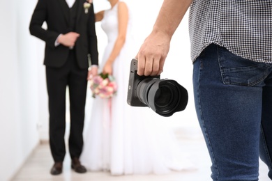 Photo of Professional photographer with camera and wedding couple in studio