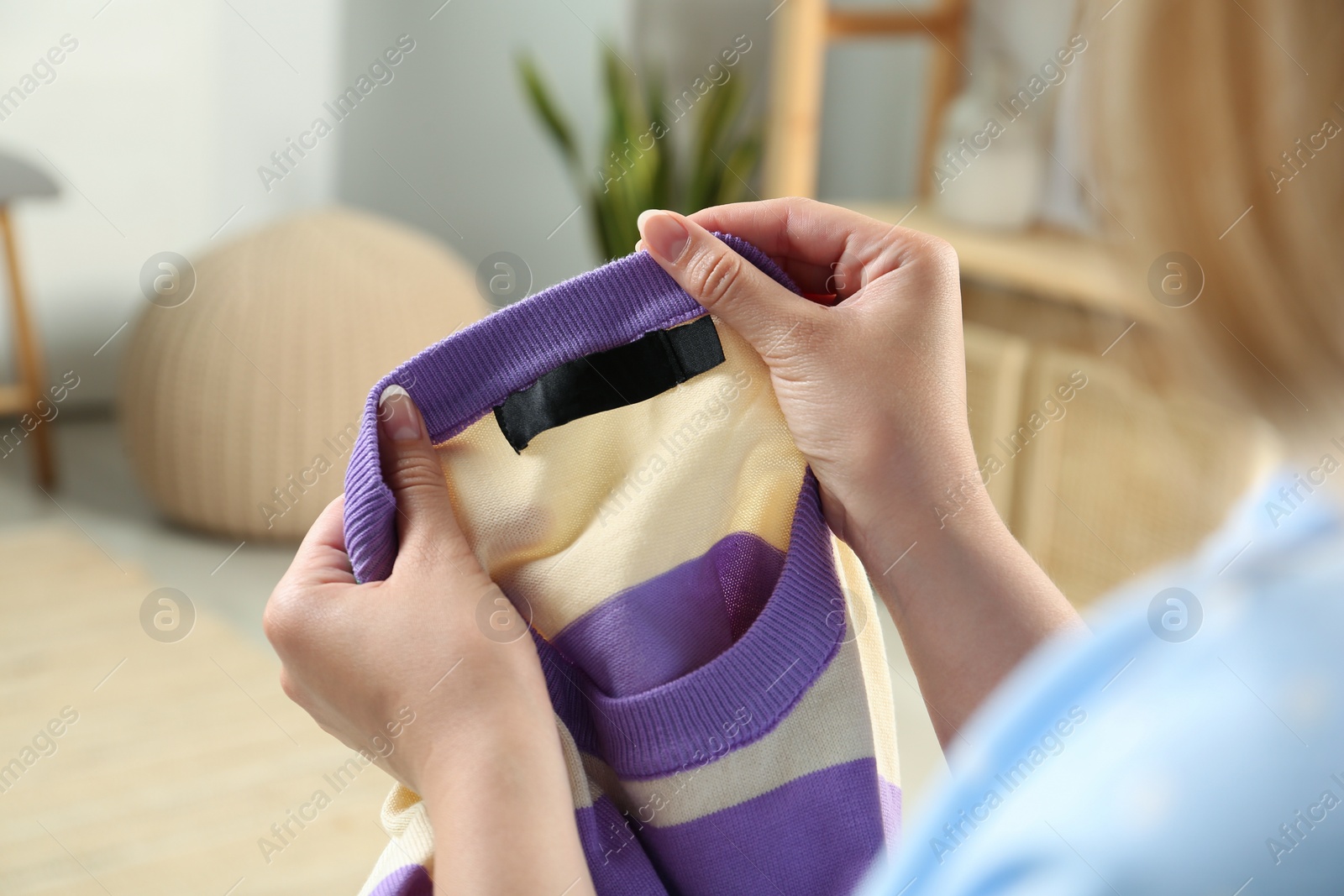 Photo of Woman holding colorful sweater with blank clothing label at home, closeup