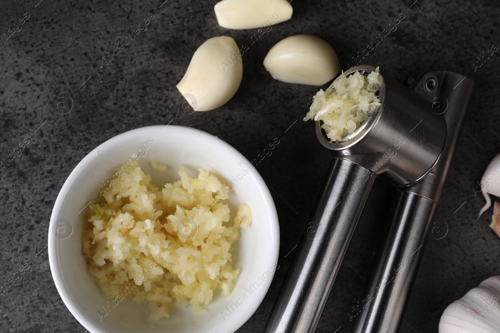 Photo of Garlic press, cloves and mince on grey table, flat lay