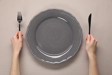 Photo of Woman with fork, knife and empty plate at gray table, top view
