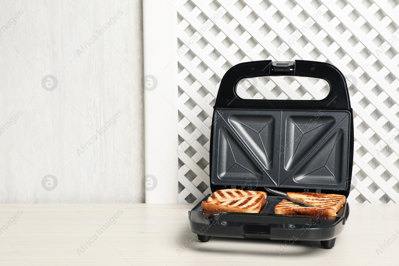 Photo of Modern sandwich maker with bread slices on white wooden table, space for text