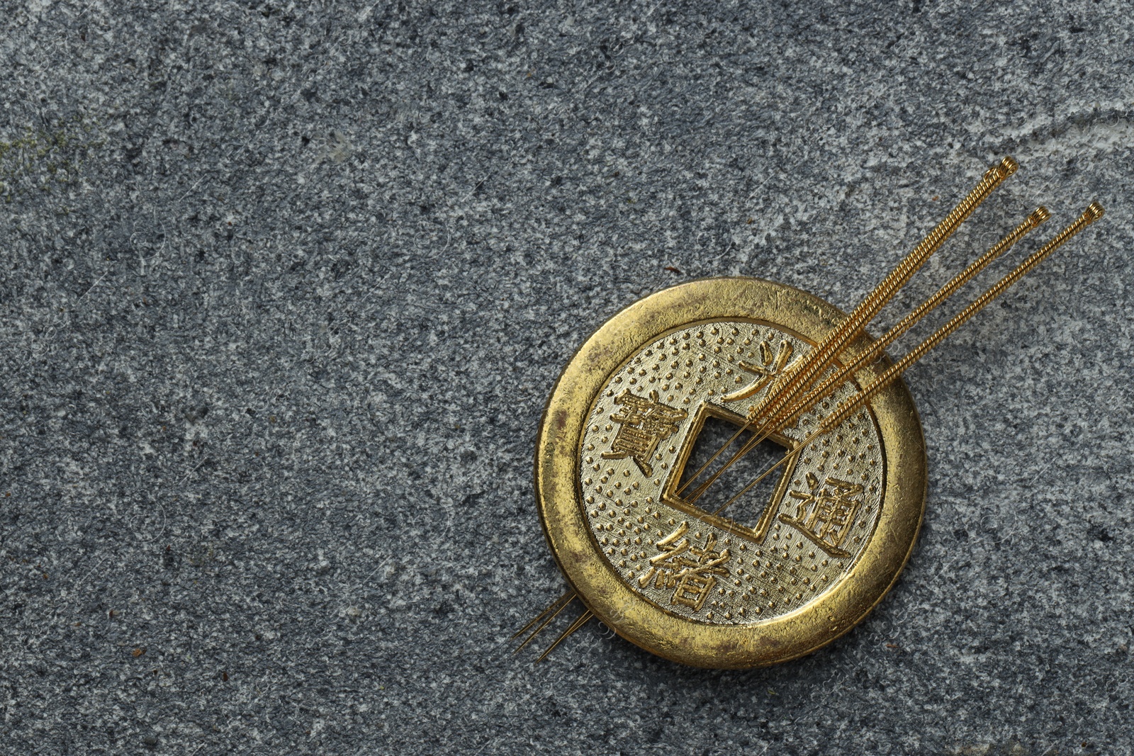 Photo of Acupuncture needles and Chinese coin on grey textured table, top view. Space for text