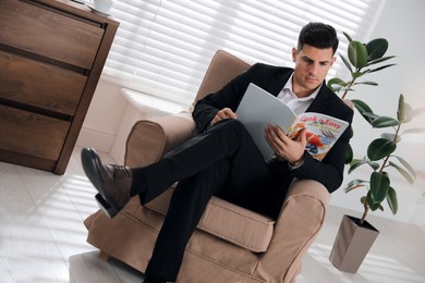 Photo of Man reading culinary magazine in armchair at home