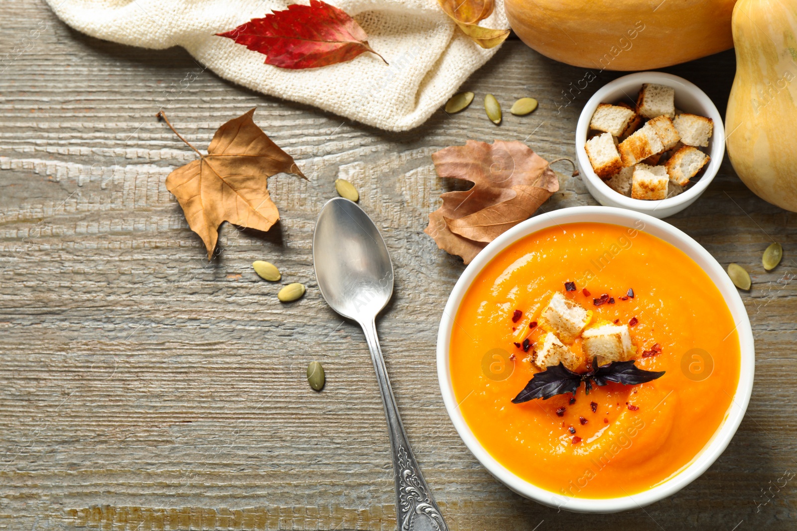 Photo of Delicious pumpkin soup in bowl on wooden table, flat lay. Space for text
