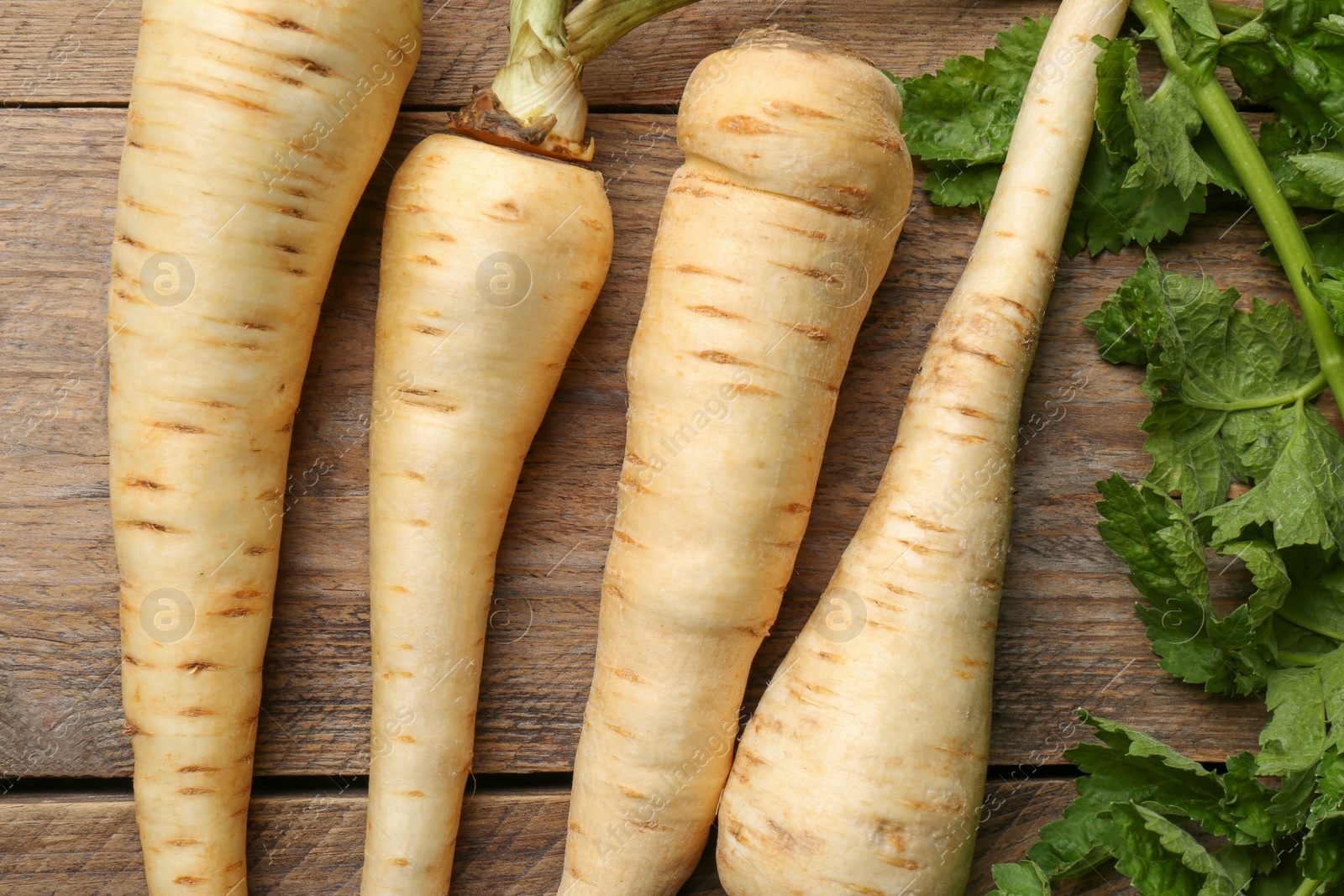 Photo of Fresh ripe parsnips with leaves on wooden table, flat lay