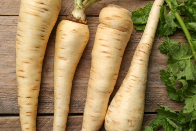 Photo of Fresh ripe parsnips with leaves on wooden table, flat lay