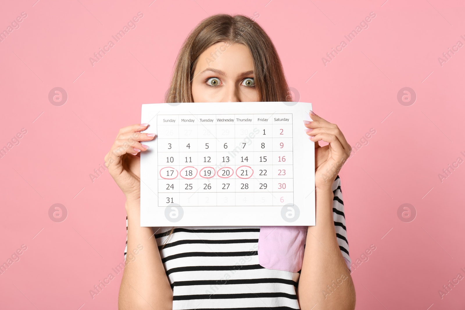 Photo of Young woman holding calendar with marked menstrual cycle days on pink background