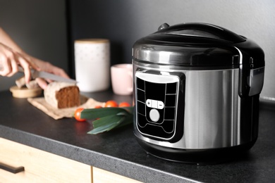 Modern multi cooker and woman slicing bread on table in kitchen, space for text