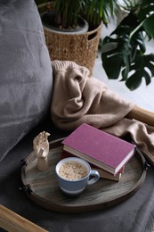 Wooden tray with books and coffee on armchair indoors