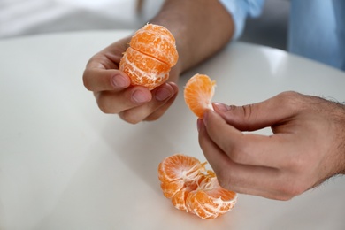 Photo of Man with fresh tangerine at table indoors, closeup