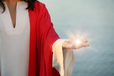 Image of Jesus Christ near water outdoors, closeup. Miraculous light in hand