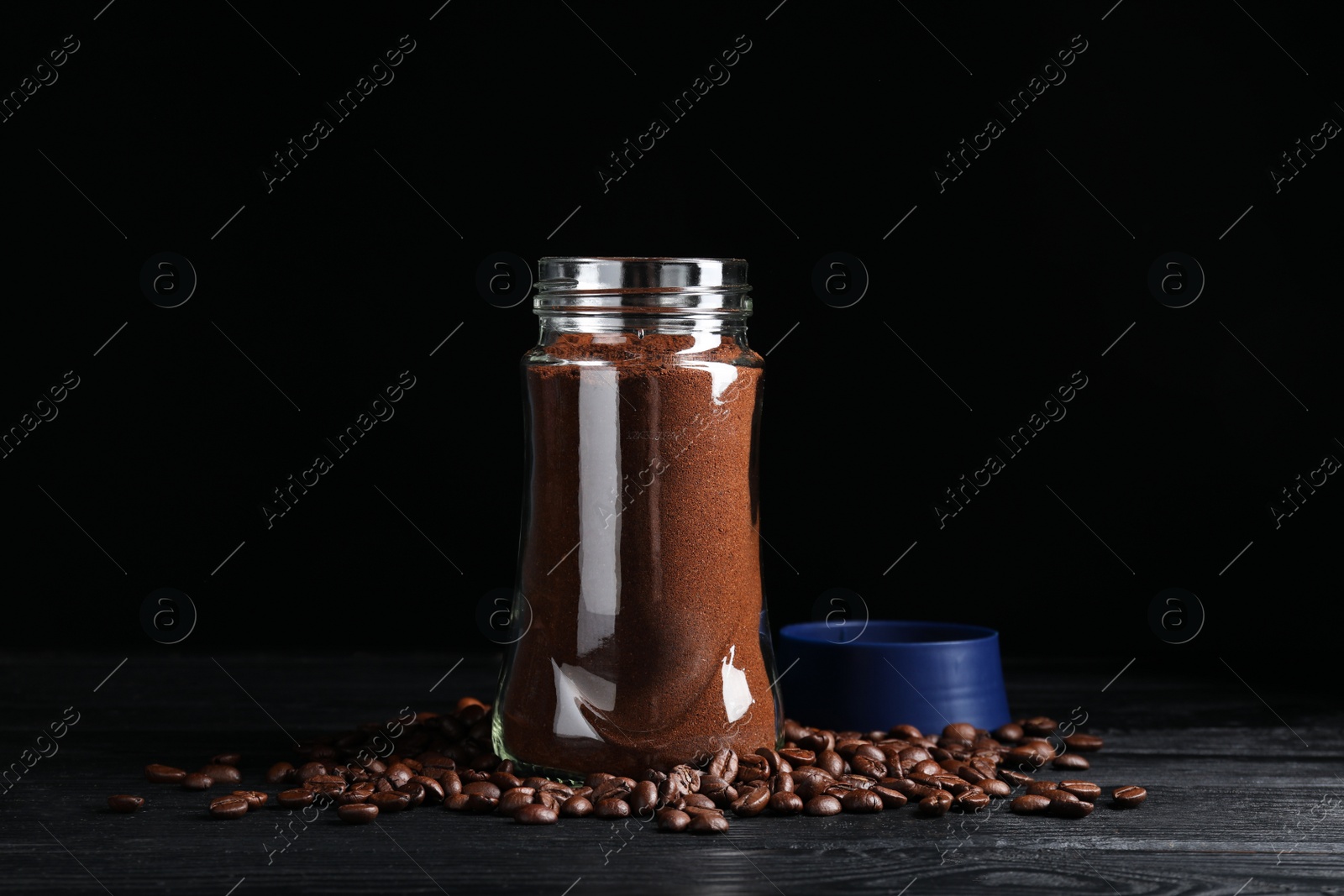Photo of Glass jar with aromatic ground coffee and beans on black wooden table