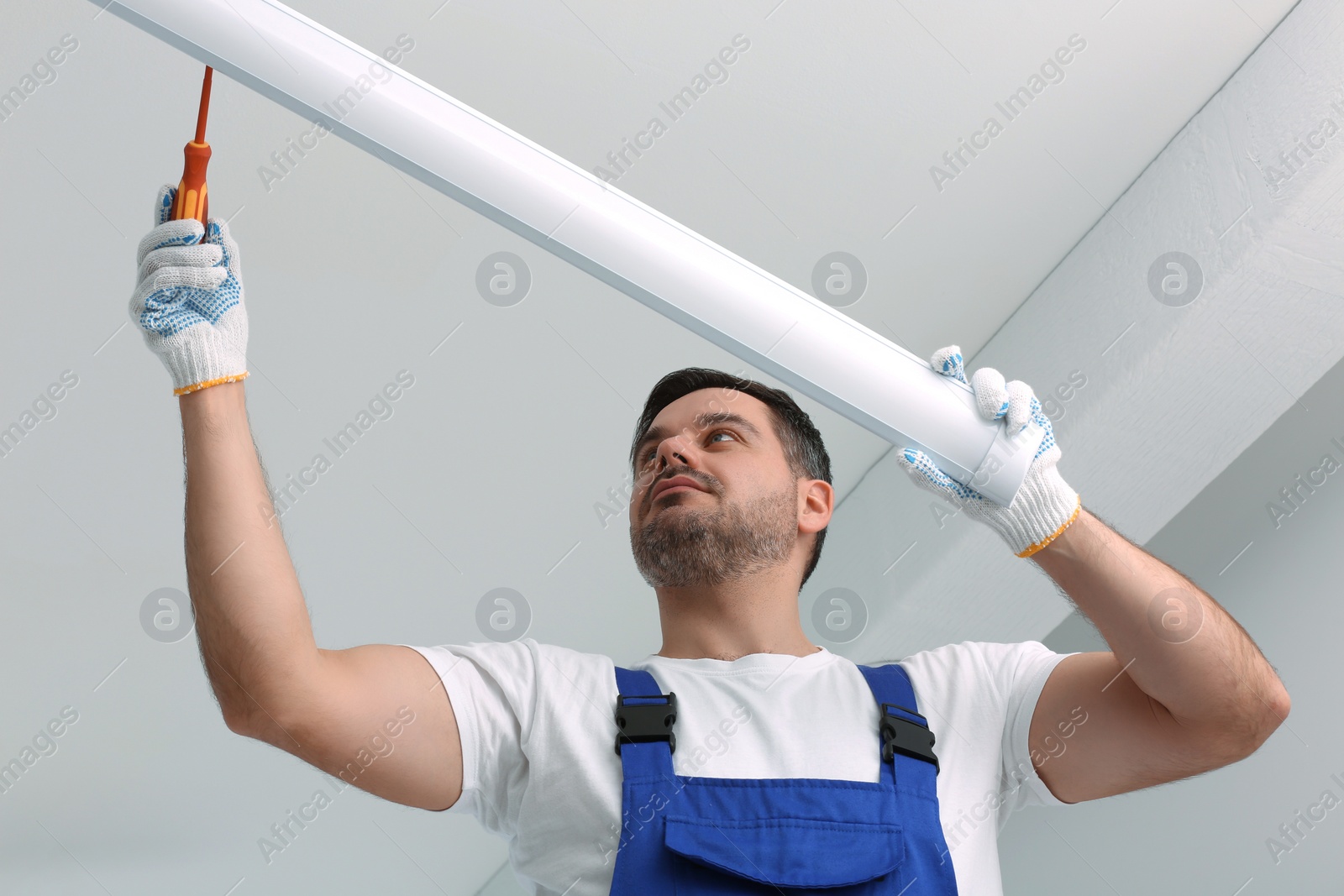 Photo of Ceiling light. Electrician installing led linear lamp indoors, low angle view