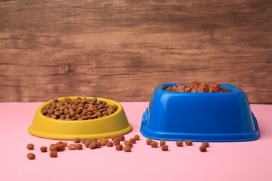 Dry and wet pet food in feeding bowls on pink table near wooden wall