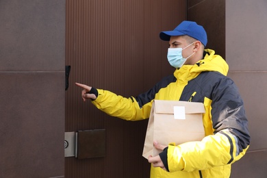 Courier in medical mask holding paper bag with takeaway food and ringing doorbell outdoors. Delivery service during quarantine due to Covid-19 outbreak