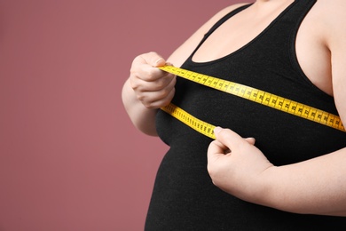 Overweight woman with measuring tape on color background