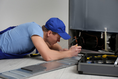 Male technician with screwdriver repairing refrigerator indoors