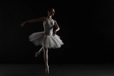 Photo of Young ballerina practicing dance moves on black background. Space for text