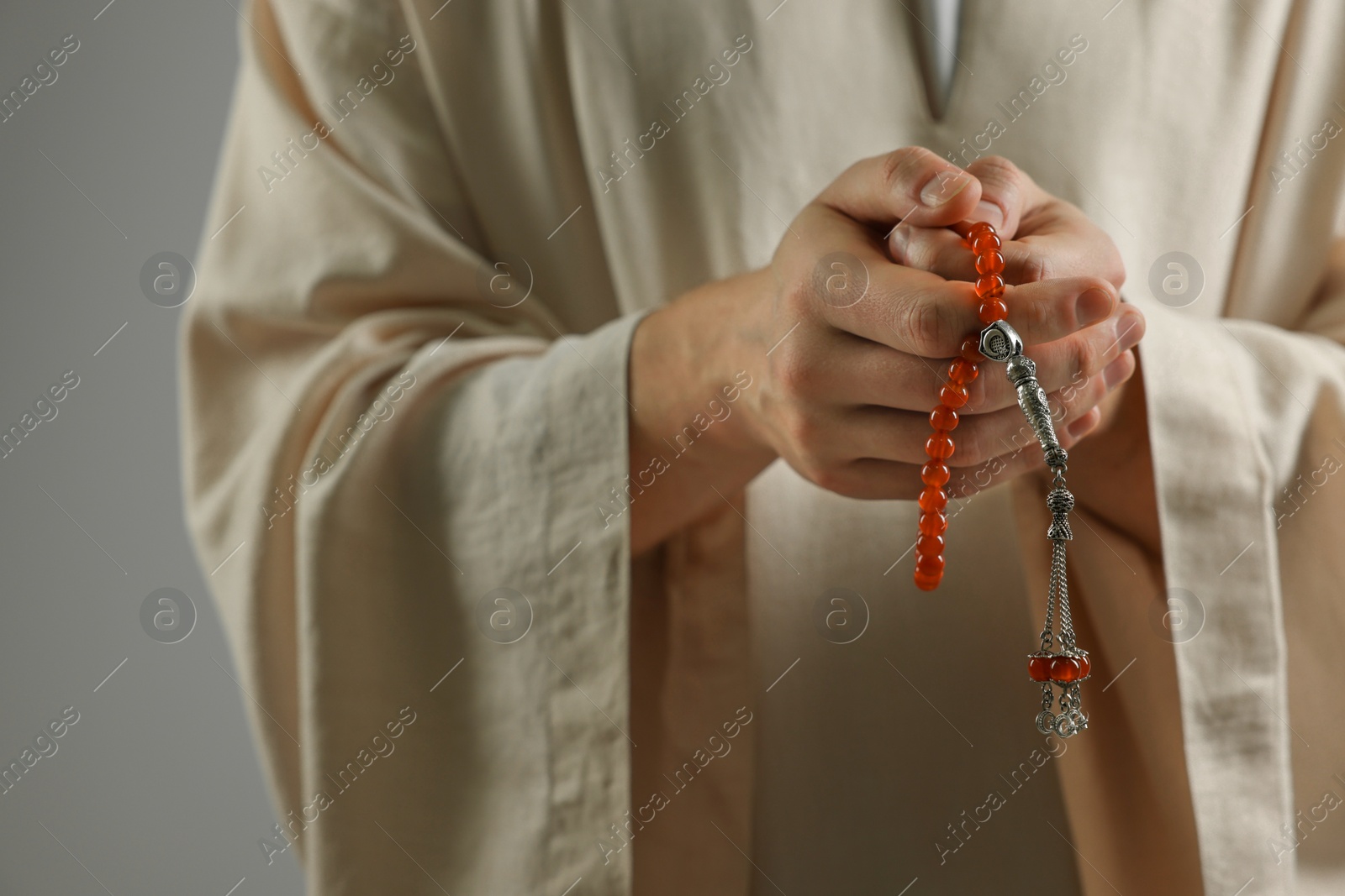 Photo of Muslim man with misbaha praying on light grey background, closeup