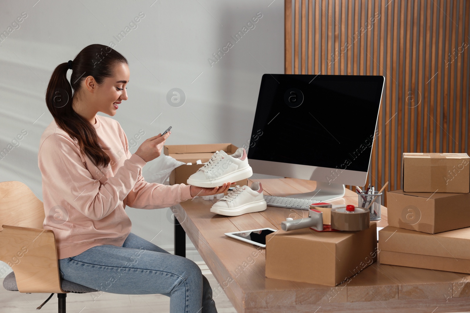 Photo of Shoes seller taking picture of sneakers at table in office. Online store
