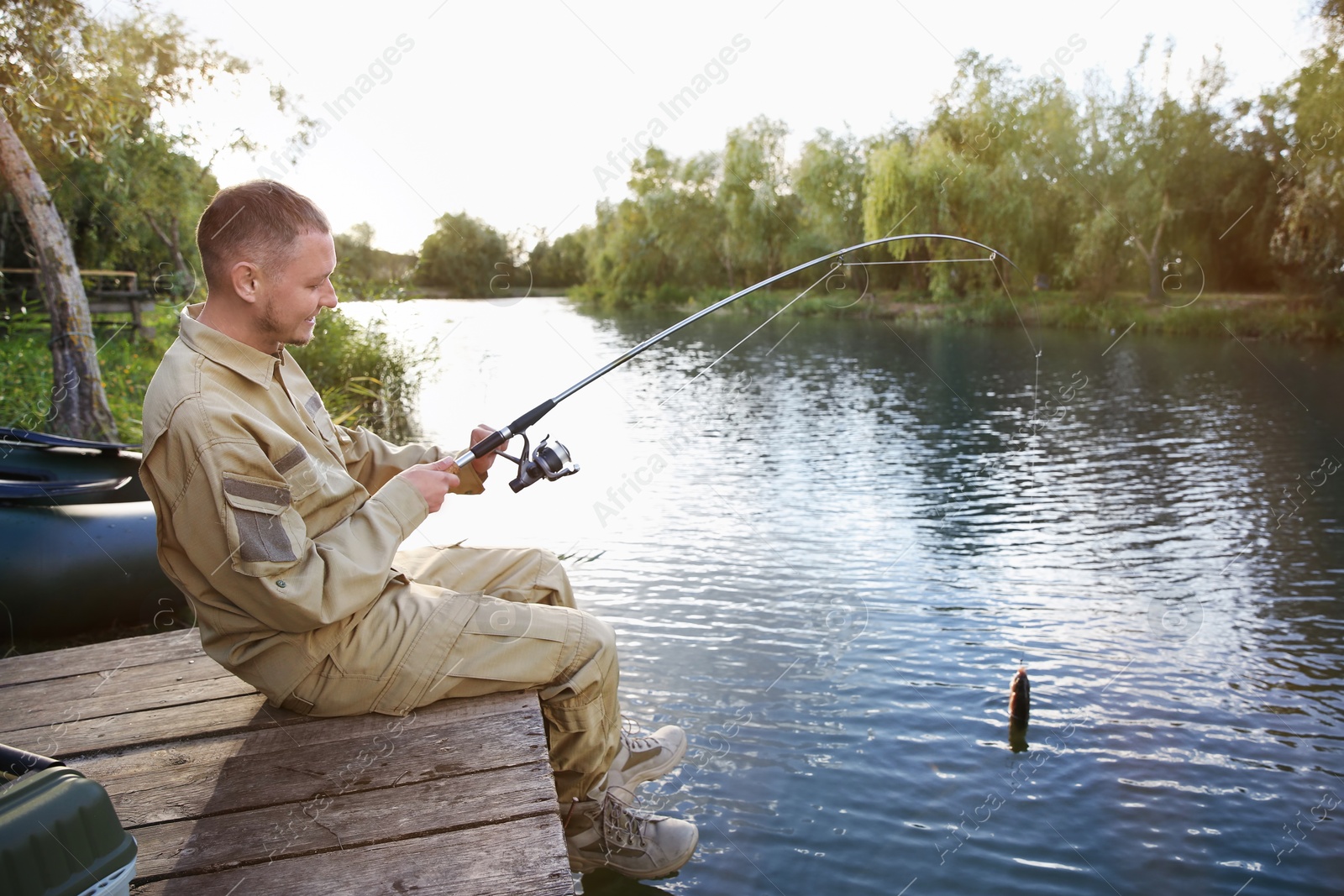 Photo of Man with rod fishing on wooden pier at riverside. Recreational activity