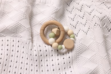 Photo of Baby accessory. Rattle on white knitted fabric, top view
