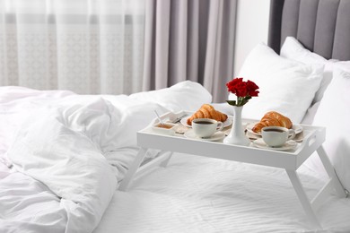 Photo of Tray with tasty breakfast and flowers on bed at home, space for text