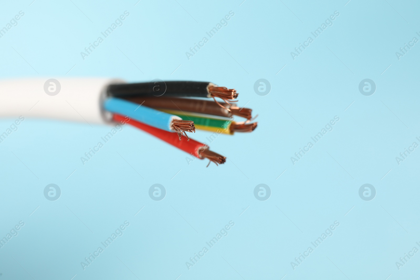 Photo of Cable with stripped electrical wires on light blue background, closeup