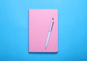 Photo of Closed pink notebook and pen on light blue background, top view