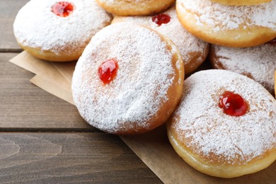 Many delicious donuts with jelly and powdered sugar on wooden table, closeup
