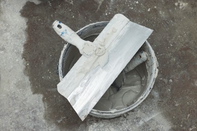Photo of Bucket with plaster and putty knives on concrete floor, top view