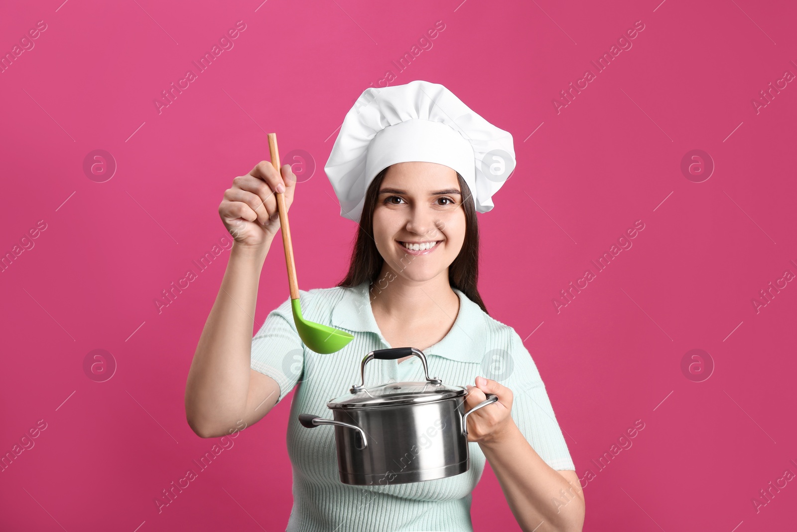 Photo of Happy young woman with cooking pot and ladle on pink background