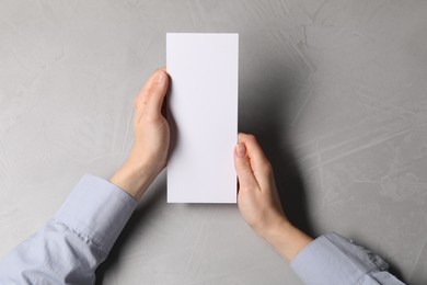 Woman holding blank card at light grey table, top view. Mockup for design