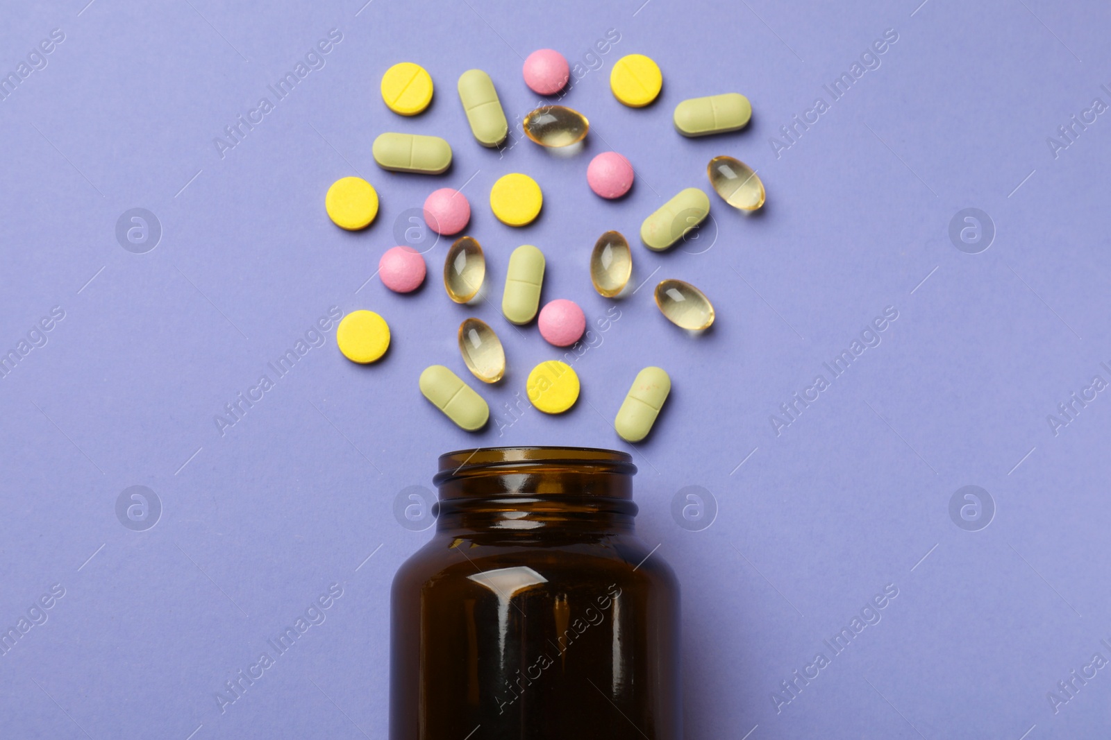 Photo of Bottle and different vitamin pills on violet background, top view