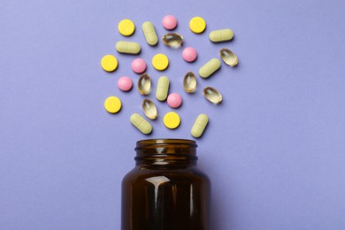 Photo of Bottle and different vitamin pills on violet background, top view