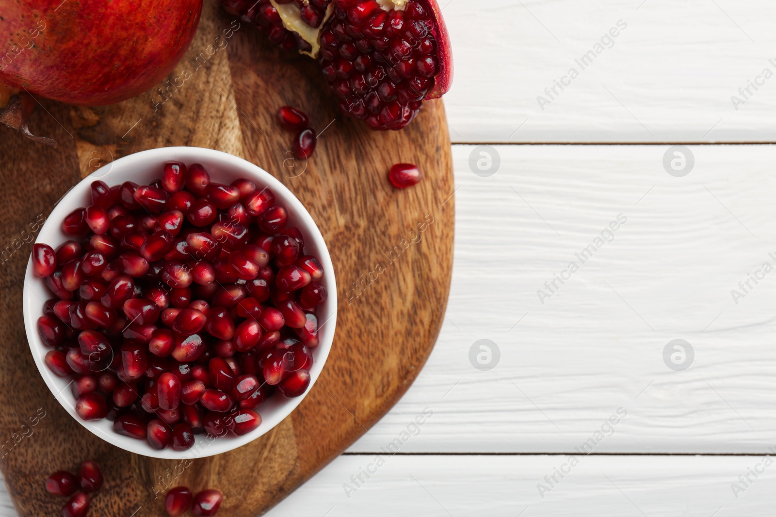 Photo of Ripe juicy pomegranate grains on white wooden table, top view. Space for text