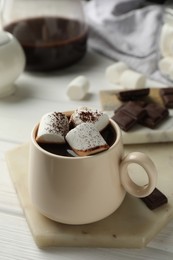 Cup of aromatic hot chocolate with marshmallows and cocoa powder on white wooden table