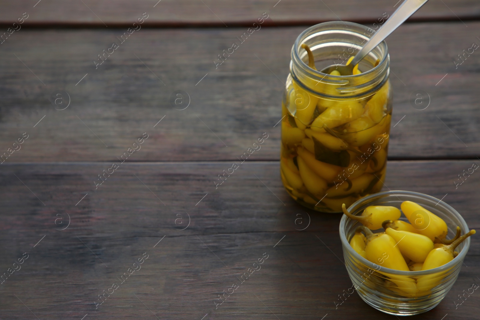 Photo of Pickled yellow jalapeno peppers on wooden table. Space for text