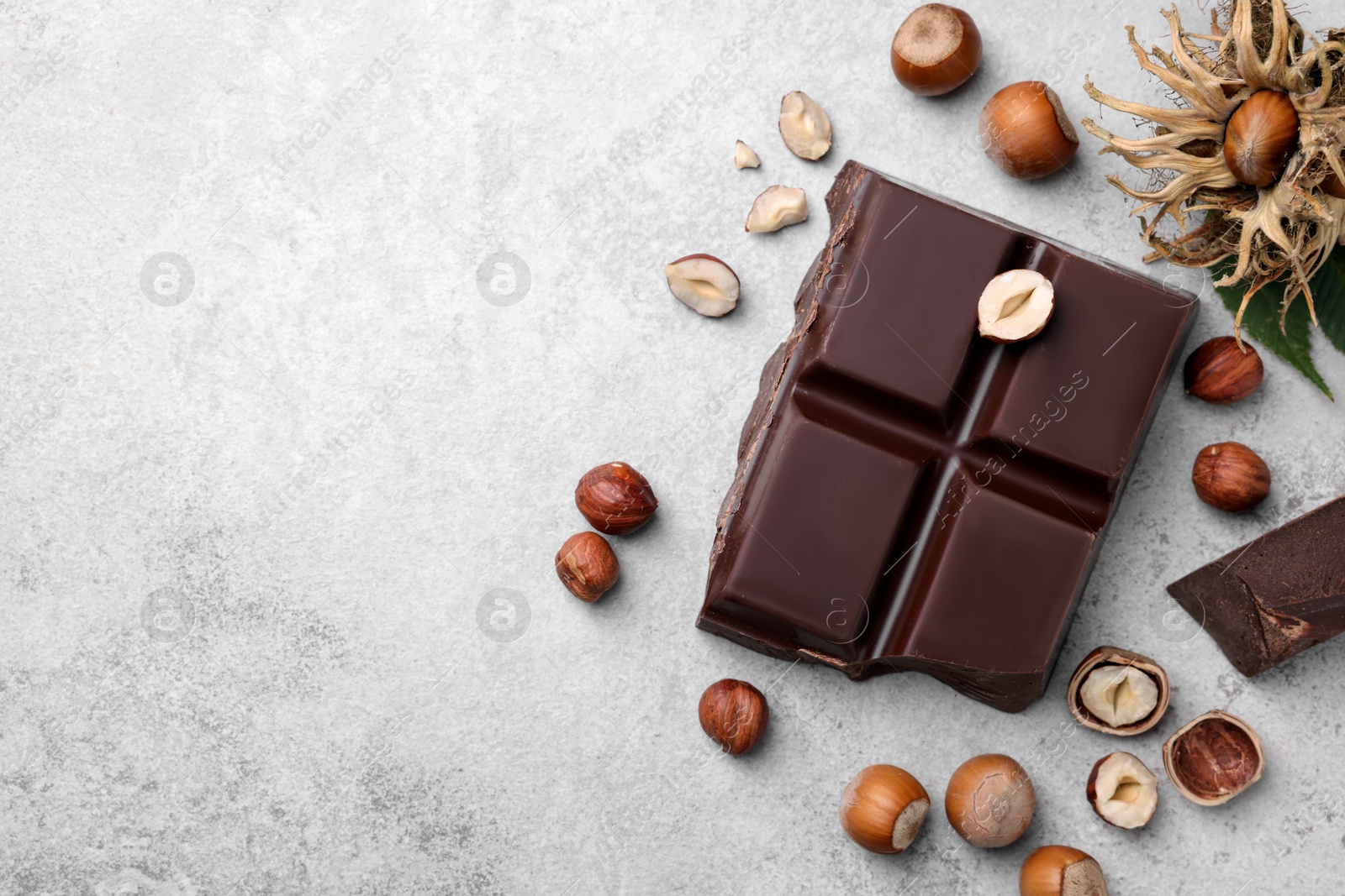 Photo of Delicious chocolate and hazelnuts on light table, flat lay. Space for text