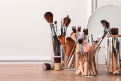 Photo of Set of professional makeup brushes and mirror on wooden table near white wall, space for text