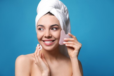 Photo of Beautiful young woman doing facial massage with gua sha tool on blue background