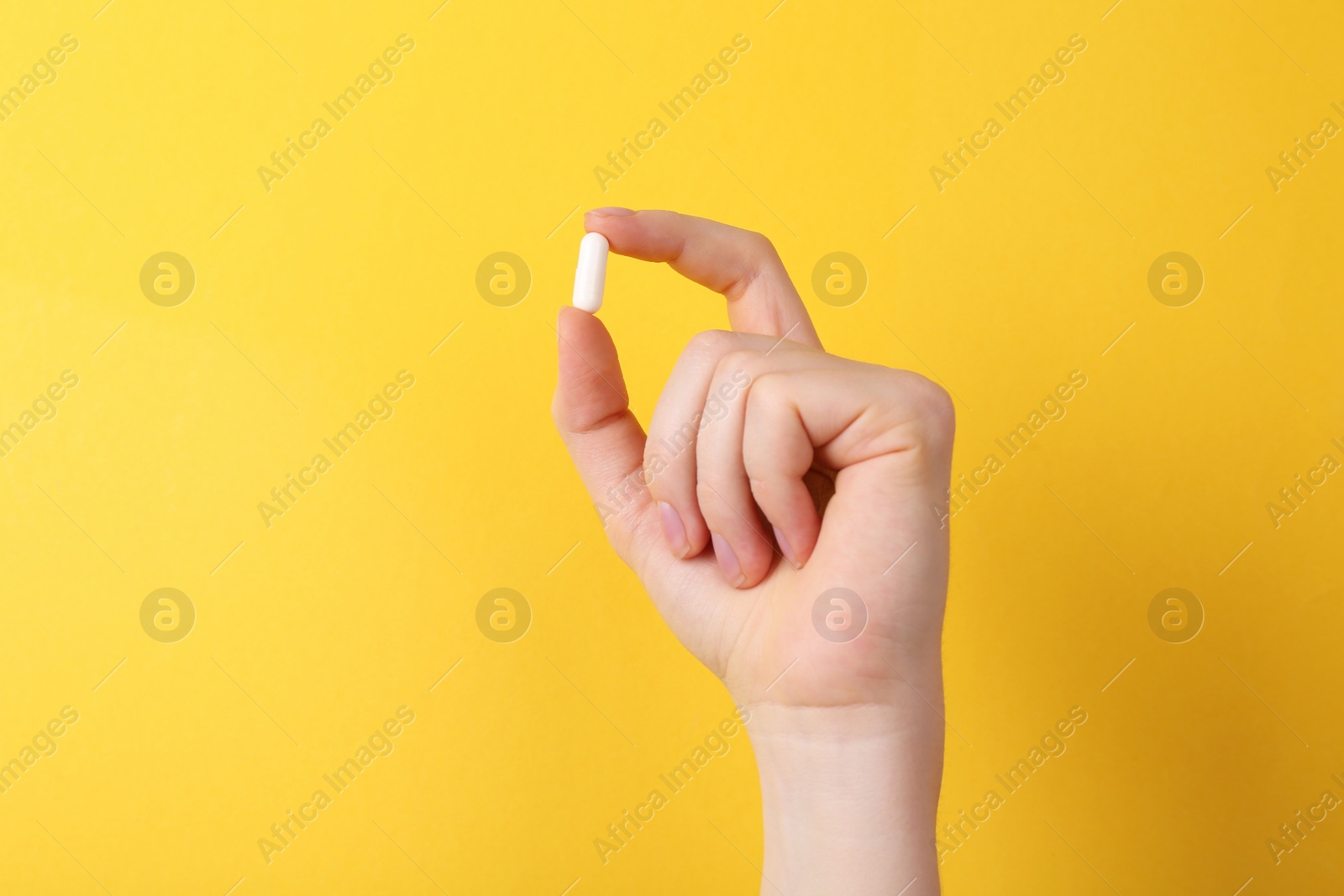 Photo of Woman holding vitamin capsule on yellow background, closeup. Space for text